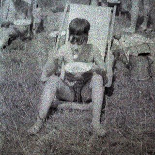 Here's a brief summary of the image: Two children sit in chairs in a grassy, blurred area.