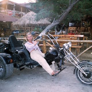 Person sits on a trike in front of a tiki bar.