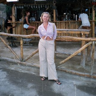 Woman stands outside a beach bar with people inside.