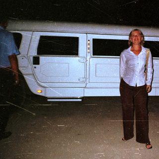 Woman stands next to a stretch limousine at night.