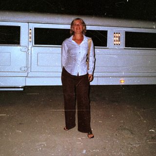 Woman stands next to a stretch limousine at night.