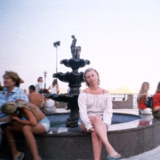 People relax around a fountain overlooking a waterfront view.