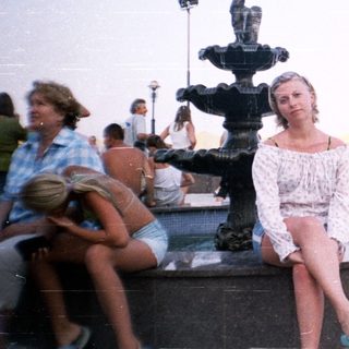 People relax around a fountain overlooking a waterfront view.