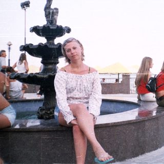 People relax around a fountain overlooking a waterfront view.