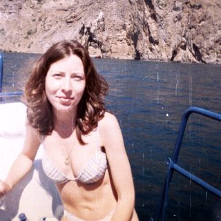 Woman in bikini on boat, scenic rock cliffs backdrop.