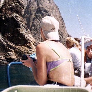Person on boat looks at phone with mountain backdrop.