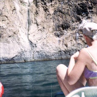 Person floats on water near a rock cliff face.
