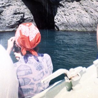 Boat approaches a rocky cliff face and cave opening.