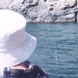 People view a rock formation from a boat on water.