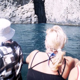 People view a rock formation from a boat on water.