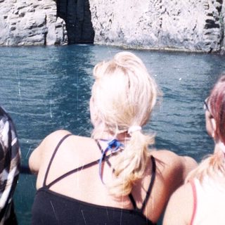 People view a rock formation from a boat on water.
