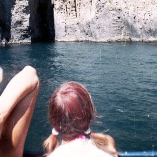 Rocky cliff face viewed from a boat, people observing.