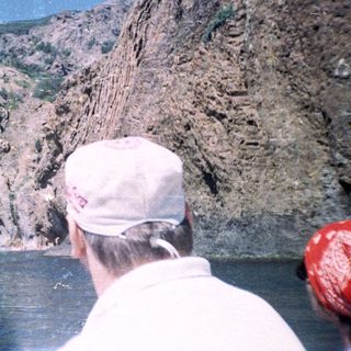 People view canyon cliffs from a boat on water.