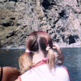 People view canyon cliffs from a boat on water.