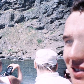 People on a boat photograph a rocky cliff face.