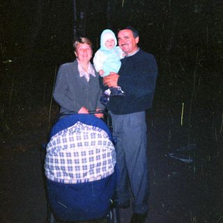 Man and woman holding baby, standing near a stroller.
