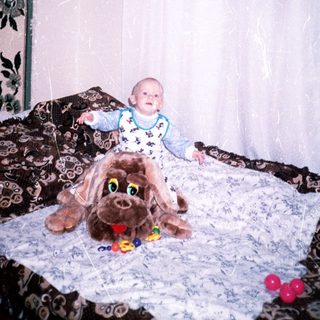 Baby sits with a large plush dog on a bed.