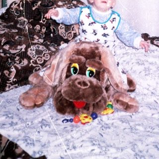 Baby sits with a large plush dog on a bed.