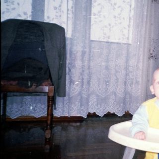 Baby sits in a high chair in a vintage room.