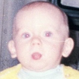 Baby sits in a high chair in a vintage room.