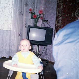 Baby sits in a high chair in a vintage room.