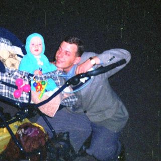 Man pushes stroller with baby at dusk near building.