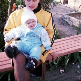 Woman and baby sit on a bench under a tree.