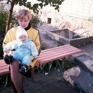 Woman and baby sit on a bench under a tree.