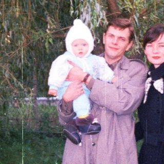 Man, woman, and baby stand outdoors near a tree.