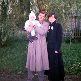 Man, woman, and baby stand outdoors near a tree.