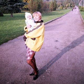 Woman holding a baby on a paved road outdoors.