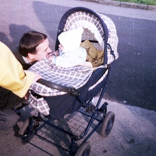 Man pushing a baby stroller along a paved path.