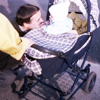 Man pushing a baby stroller along a paved path.