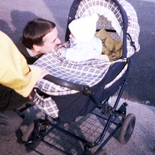 Man pushing a baby stroller along a paved path.