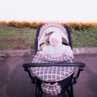 Baby in a stroller sits outdoors on a paved path.