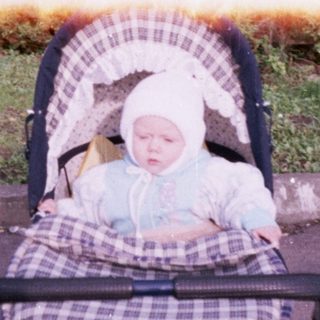 Baby in a stroller sits outdoors on a paved path.