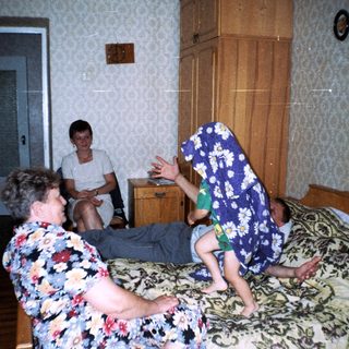 A boy jumps on a bed while others watch.