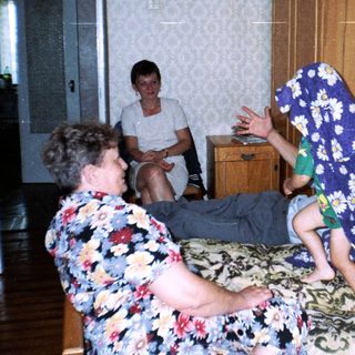 A boy jumps on a bed while others watch.