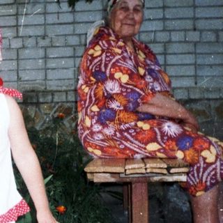 Child stands near an elderly woman in a garden.