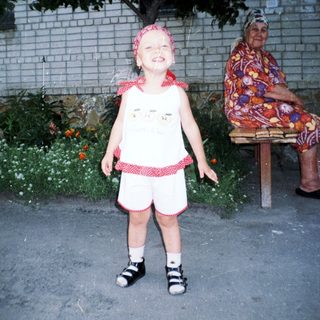 Child stands near an elderly woman in a garden.
