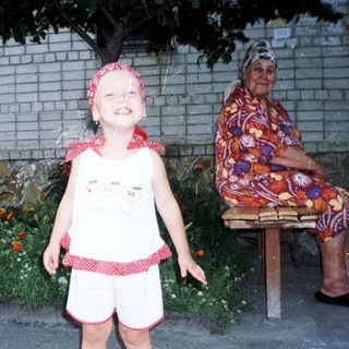 Child stands near an elderly woman in a garden.