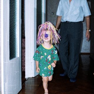 Here's a brief summary of the image: Child with a wig runs, followed by an adult.