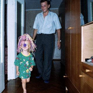 Here's a brief summary of the image: Child with a wig runs, followed by an adult.