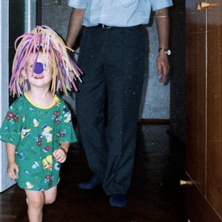 Here's a brief summary of the image: Child with a wig runs, followed by an adult.