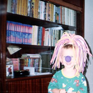 Child with a wig stands near a seated man.