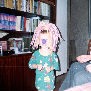 Child with a wig stands near a seated man.