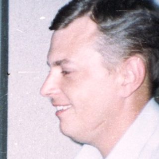 Child with a wig stands near a seated man.