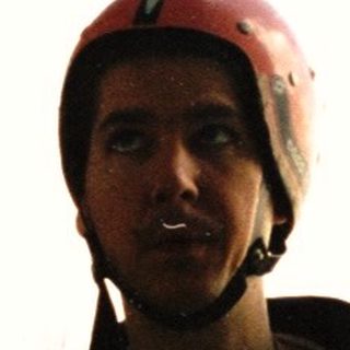 Man wearing a helmet stands near a rock climbing rope.