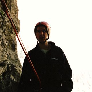 Man wearing a helmet stands near a rock climbing rope.