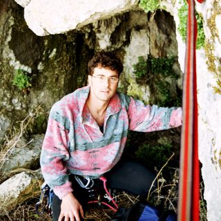 Man sits beneath rock overhang, possibly rock climbing.
